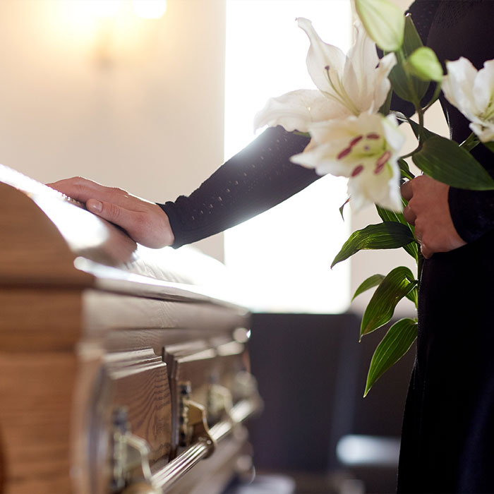 Pompes funèbres LOIC - Photo d'un cercueil et une main de femme posée, l'autre tenant un bouquet