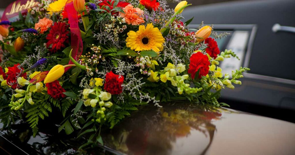 Pompes Funèbres Loic - Boutique funéraire - Cercueil funéraire et fleurs à côté du corbillard
